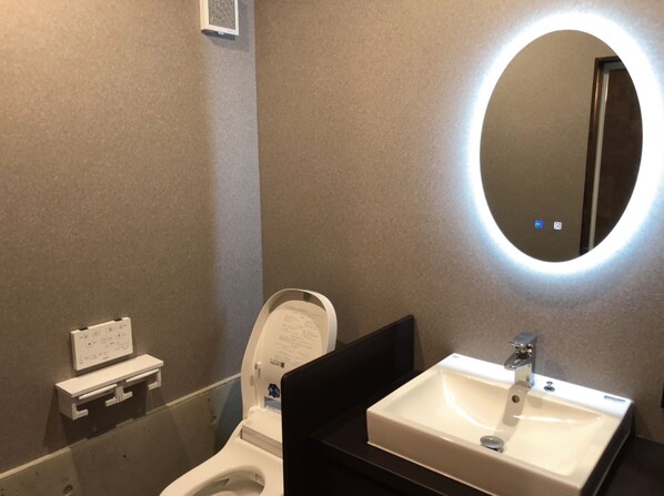 Un baño moderno con inodoro, lavamanos y espejo con luz circular.