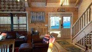 A wooden cabin interior with a sofa, armchair, and a staircase. - Breathtaking Norris Lake Mountain Retreat (New Tazewell)
