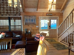 Ein Holzblockhaus-Innenraum mit Sofa, Sesseln und einer Treppe.