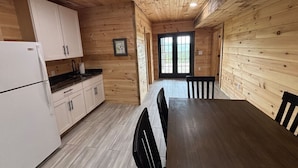 A wooden interior with a kitchen, dining table, chairs, and a door leading outside. - Breathtaking Norris Lake Mountain Retreat (New Tazewell)