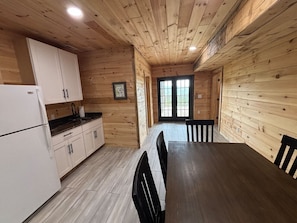 Ein Holzinterieur mit einer Küche, einem Esstisch, Stühlen und einer zur Außenseite führenden Tür.