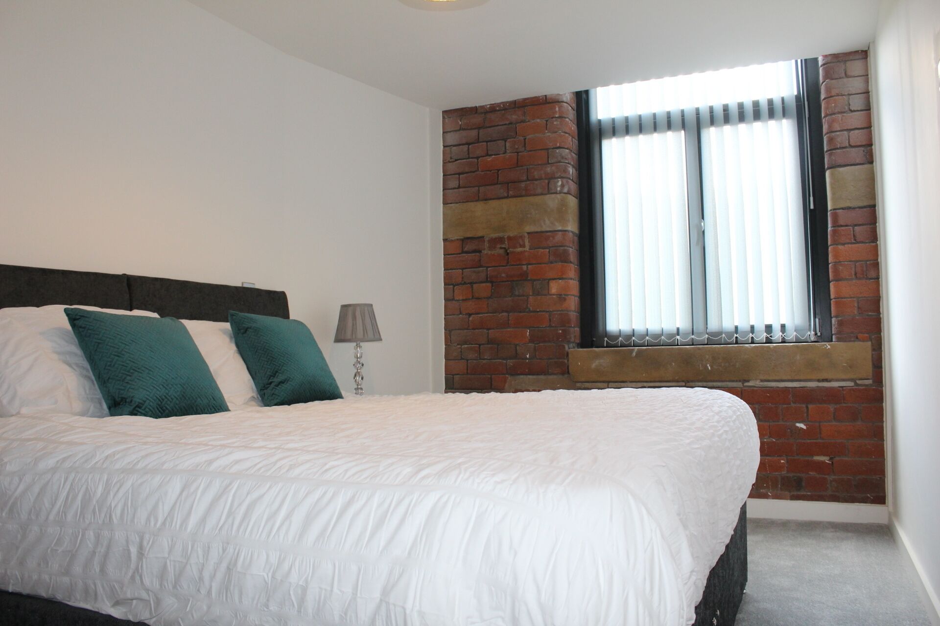 A bedroom with a bed, a nightstand, a lamp, and a window with blinds.