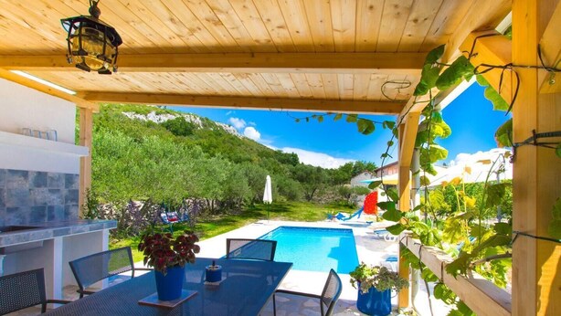 Ein überdachter Außenbereich mit Pool, Sitzgelegenheiten und Blick auf die grüne Umgebung.