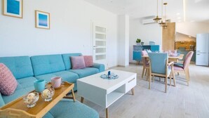Ein modernes Wohnzimmer mit einem blauen Sofa, einem Esstisch mit Stühlen und einer Küche im Hintergrund.