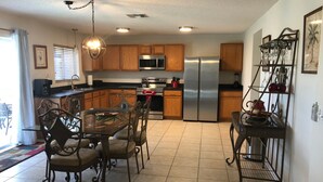 A modern kitchen with wooden cabinets, stainless steel appliances, a dining table with chairs, and a decorative metal shelf.