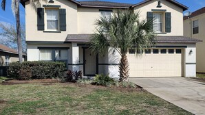 A two-story house with a garage, a palm tree, and a well-maintained lawn.