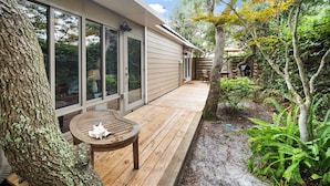 Une terrasse en bois avec une table et des chaises, entourée d’arbres et d’un jardin.