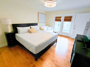 Quarto com cama, mesas de cabeceira, abajur, cômoda, espelho e porta com vista.