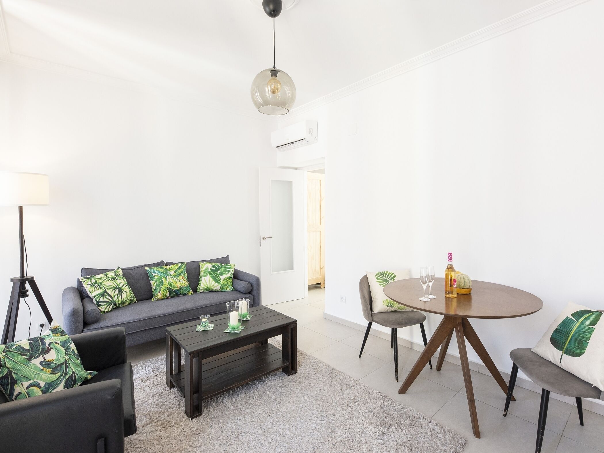 Ein modernes Wohnzimmer mit einem grauen Sofa, einem Couchtisch, einem Esstisch mit Stühlen und einer Pendelleuchte.