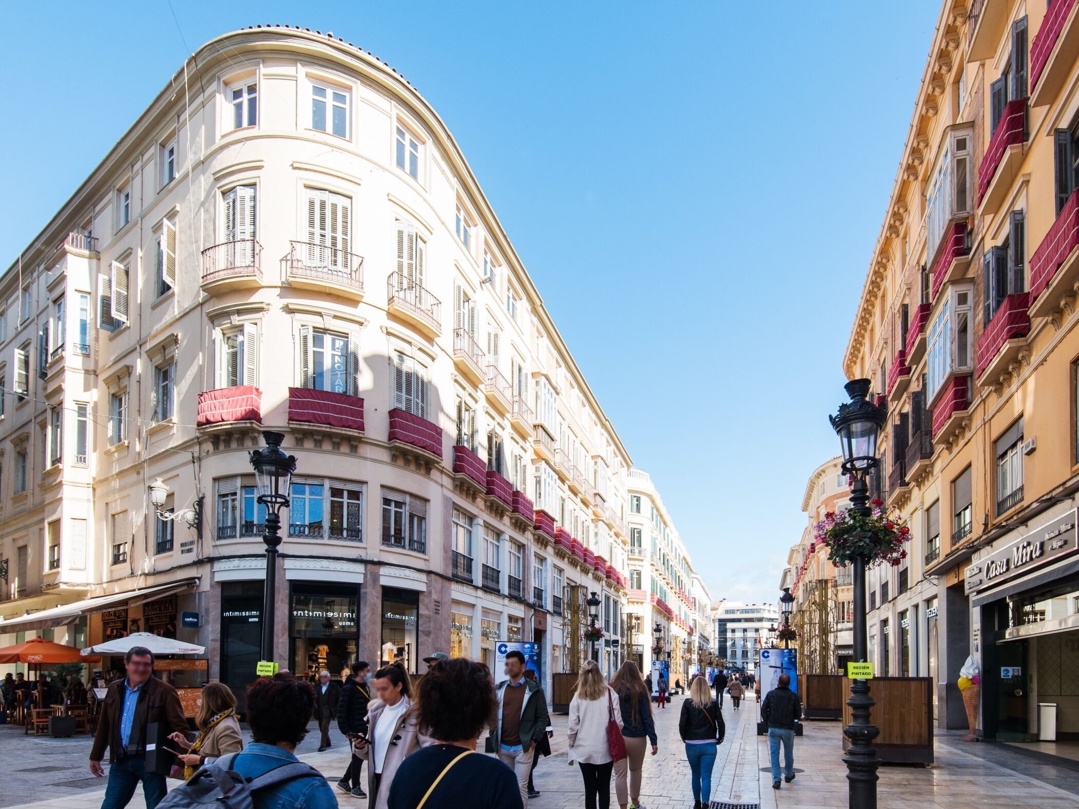 Ruas com edifícios históricos, lojas e pessoas caminhando.