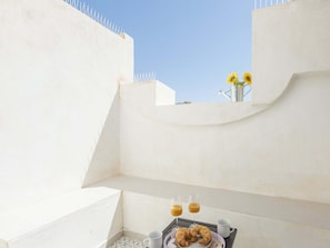 A rooftop terrace with a table set for breakfast, including croissants and drinks, and a vase with sunflowers.