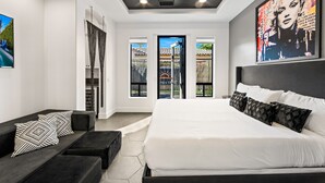 Un dormitorio moderno con una cama grande, un sofá negro y un cuadro en la pared.
