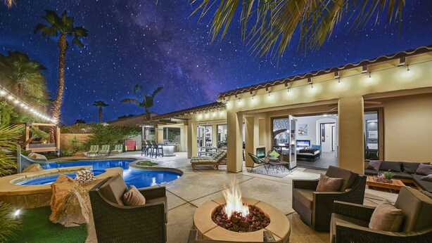 Un área de piscina con una chimenea, mobiliario exterior y un porche cubierto.