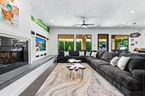 A modern living room with a sectional sofa, a fireplace, and a large TV screen.
