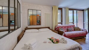 Quarto de hotel com uma cama grande, um sofá menor, um espelho e uma janela com cortinas.