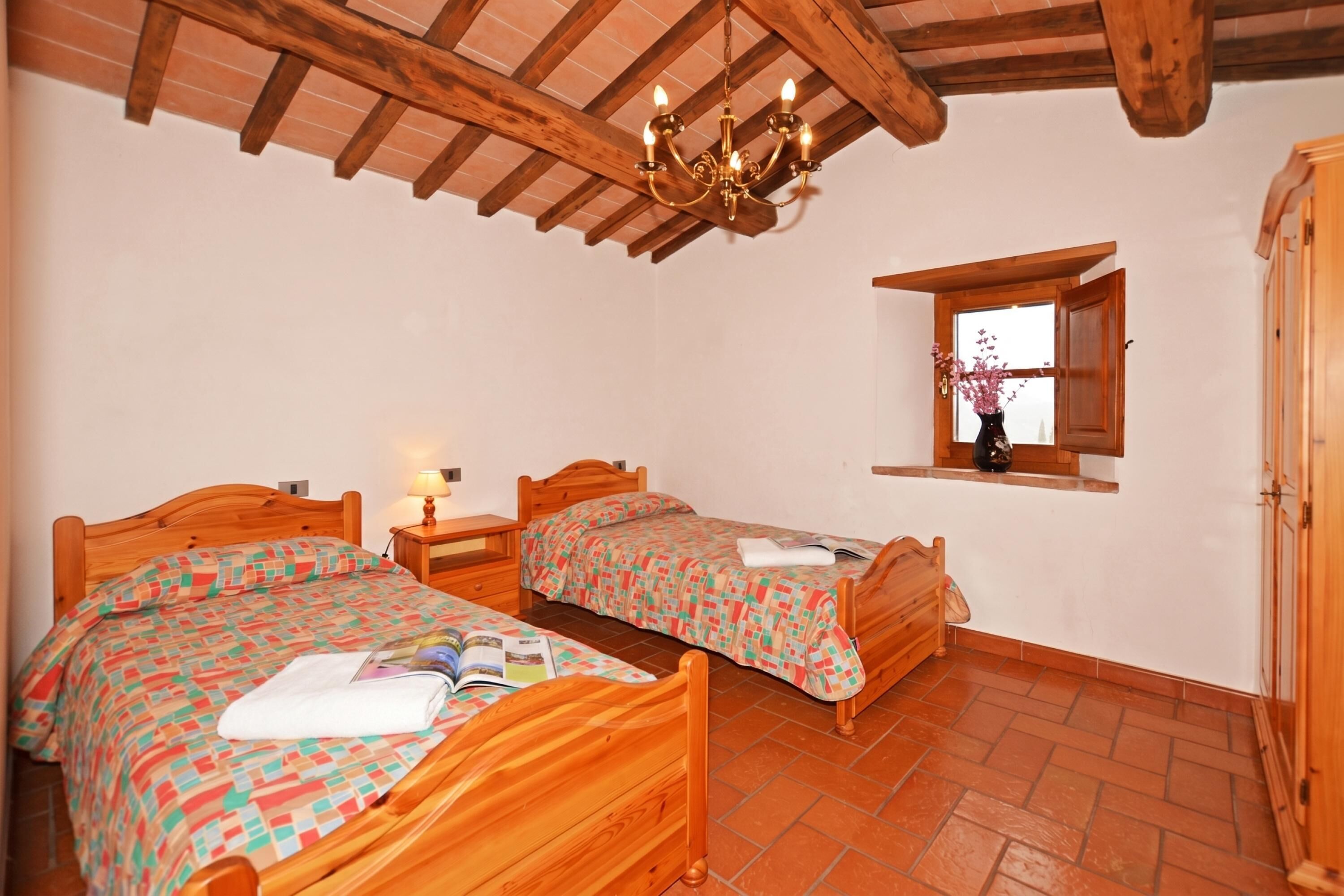 A bedroom with two wooden beds, a chandelier, a window with a view, and a wooden wardrobe.