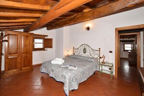 A bedroom with a wooden ceiling, a bed with a patterned bedspread, a bedside table with a lamp, and a wardrobe. - Villa La Chiesina, Arcidosso, Italy (Arcidosso)