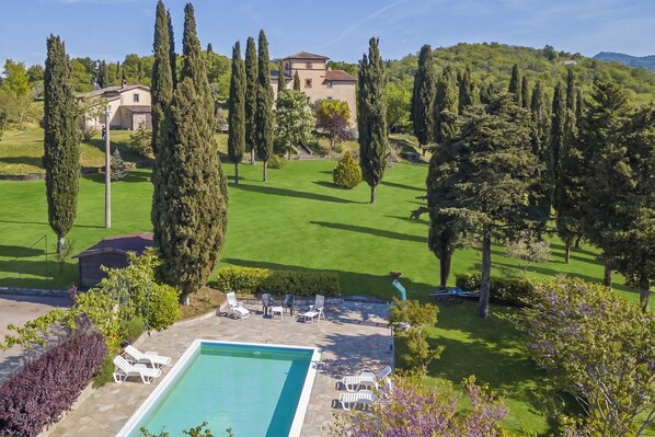 A pool with lounge chairs, a stone patio, and a large house with a garden in the background. - Villa La Chiesina, Arcidosso, Italy (Arcidosso)