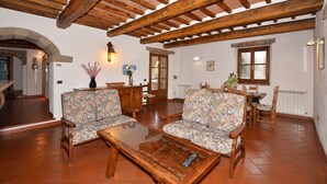 Ein gemütliches Wohnzimmer mit Holzbalken, gemusterten Sofas, einem Couchtisch und einem Essbereich mit Stühlen und einem Tisch.