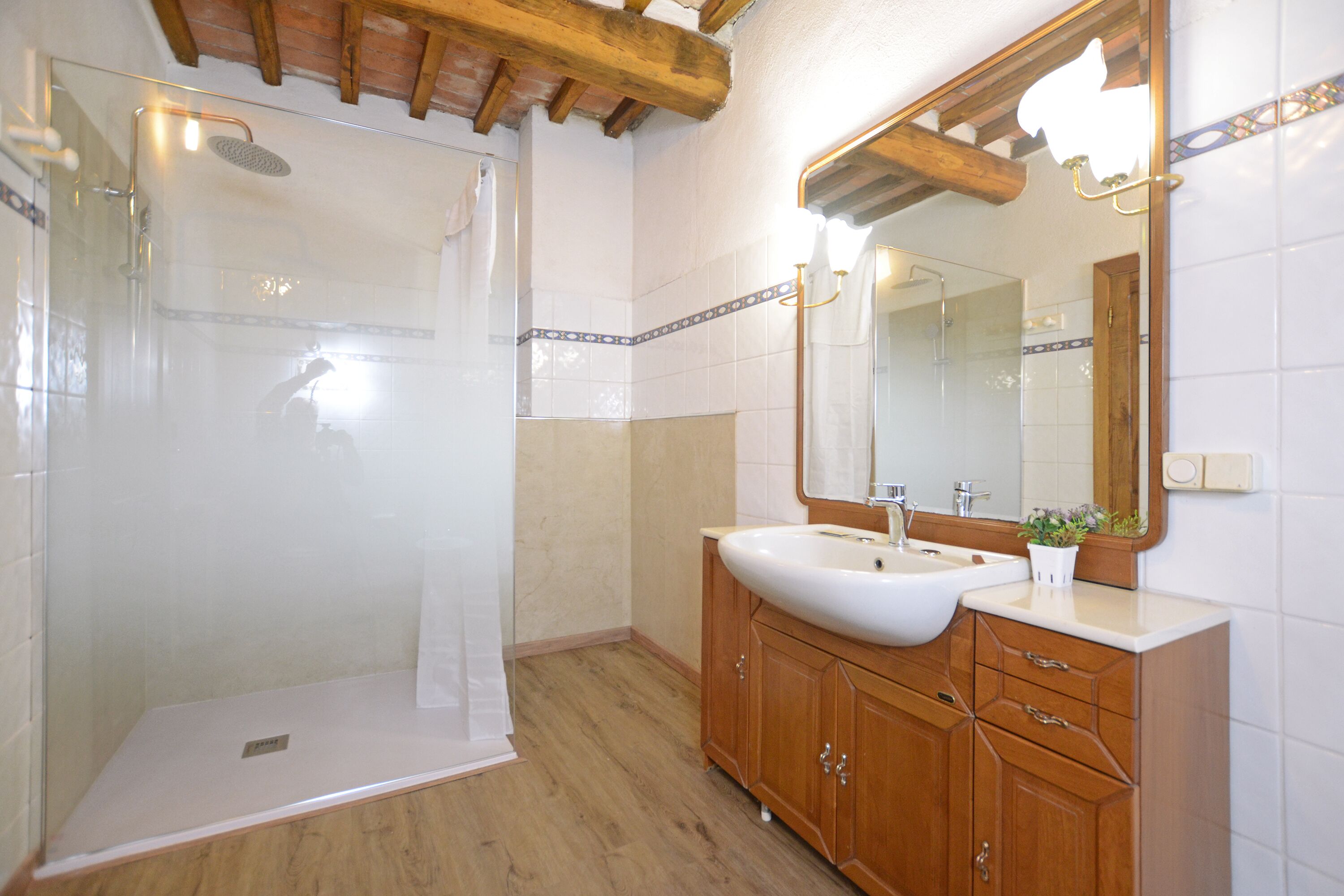 A bathroom with a glass-enclosed shower, a large mirror, and wooden cabinetry.