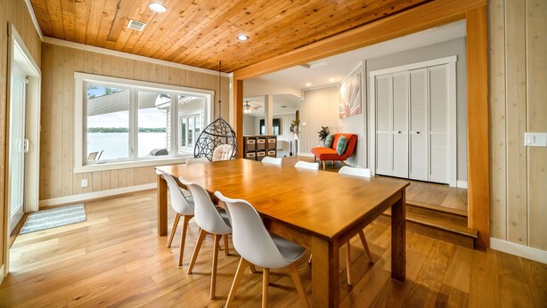 A spacious dining area with a wooden table and chairs, large windows, and a view of the outdoors.