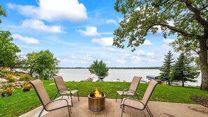 A patio with two chairs and a fire pit overlooking a lake.