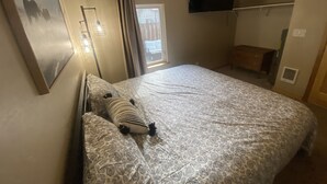 Une chambre à coucher comprenant un lit, un téléviseur à écran plat fixé au mur, une table de chevet et une fenêtre avec des rideaux.
