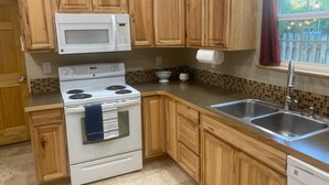 Une cuisine avec des meubles en bois, une cuisinière blanche, un four à micro-ondes, un évier et une fenêtre donnant sur un paysage verdoyant.