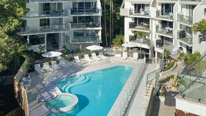 Un hotel moderno con piscina en la azotea, varios balcones y zonas de estar al aire libre.