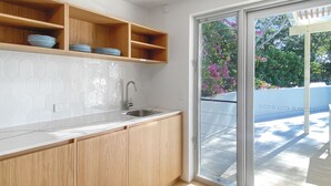 Una cocina moderna con armarios de madera, encimera de mármol y un amplio ventanal corredero que da a un espacio exterior.