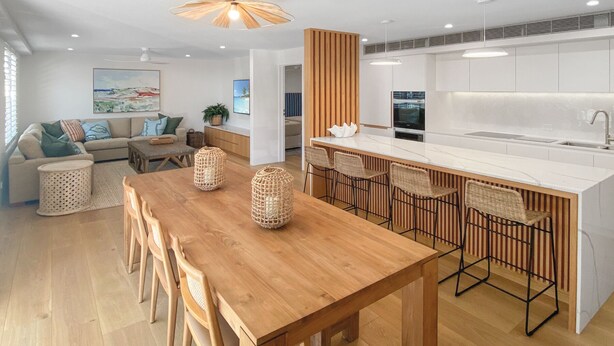 Una cocina moderna con una mesa de comedor de madera y taburetes de bar, una isla grande y una sala de estar con sofá y obras de arte.