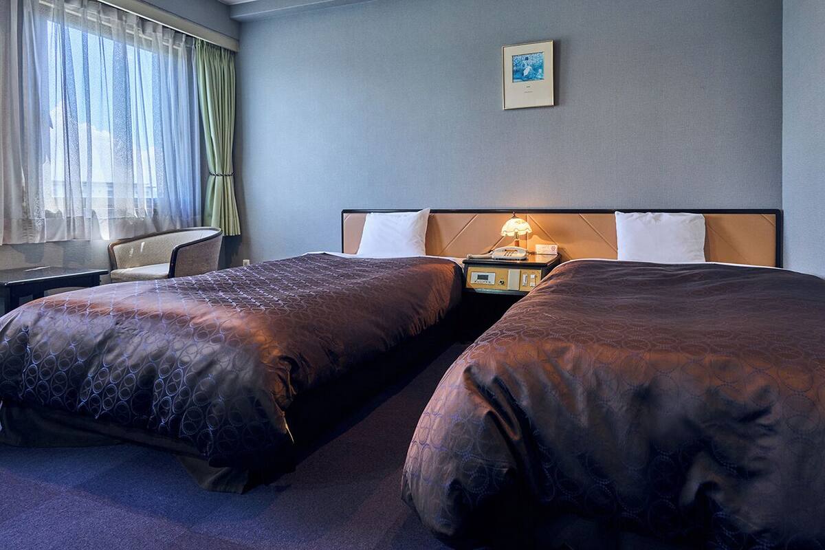 A hotel room with two beds, a bedside table with a lamp, and a framed picture on the wall.