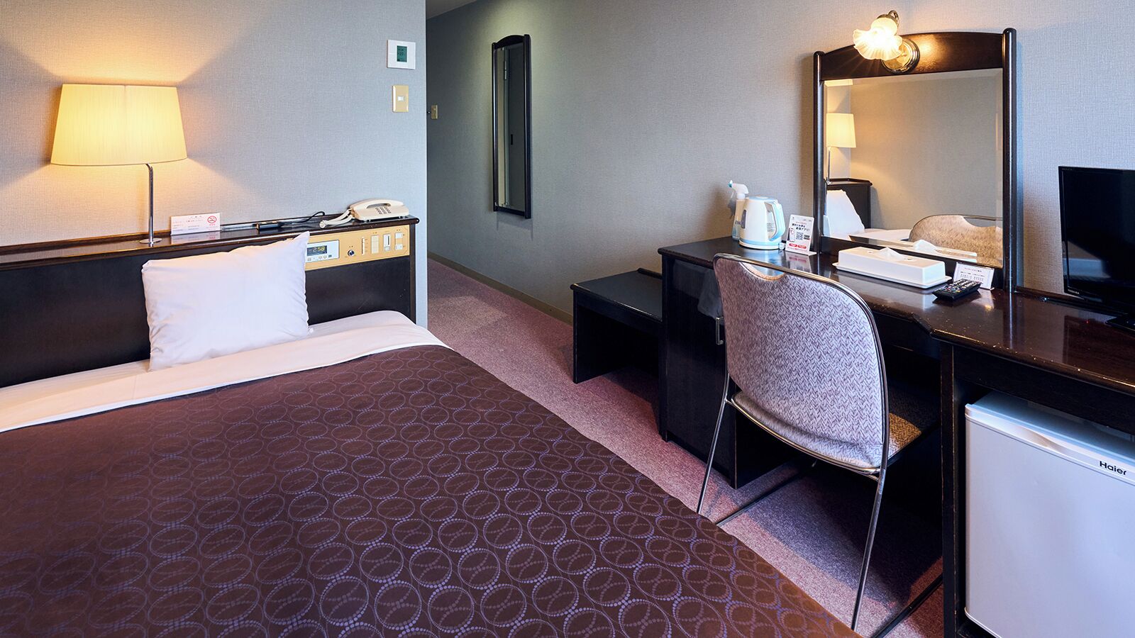 Une chambre d’hôtel équipée d’un lit, d’un bureau, d’une chaise et d’un petit réfrigérateur.