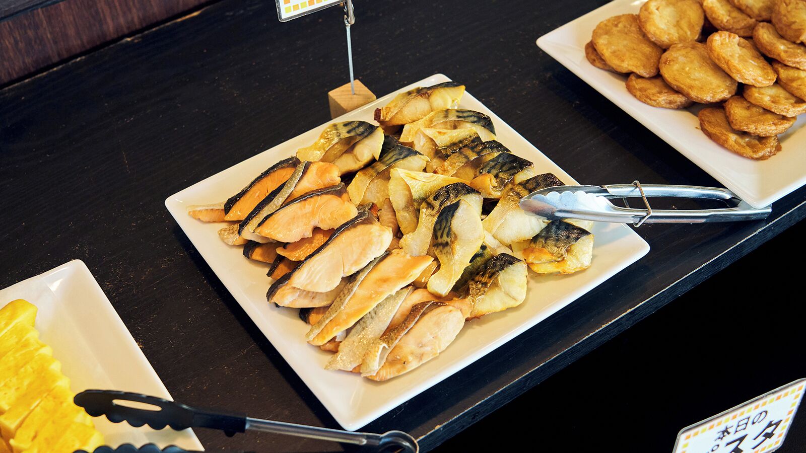 A buffet with various food items including sliced fish and pastries.