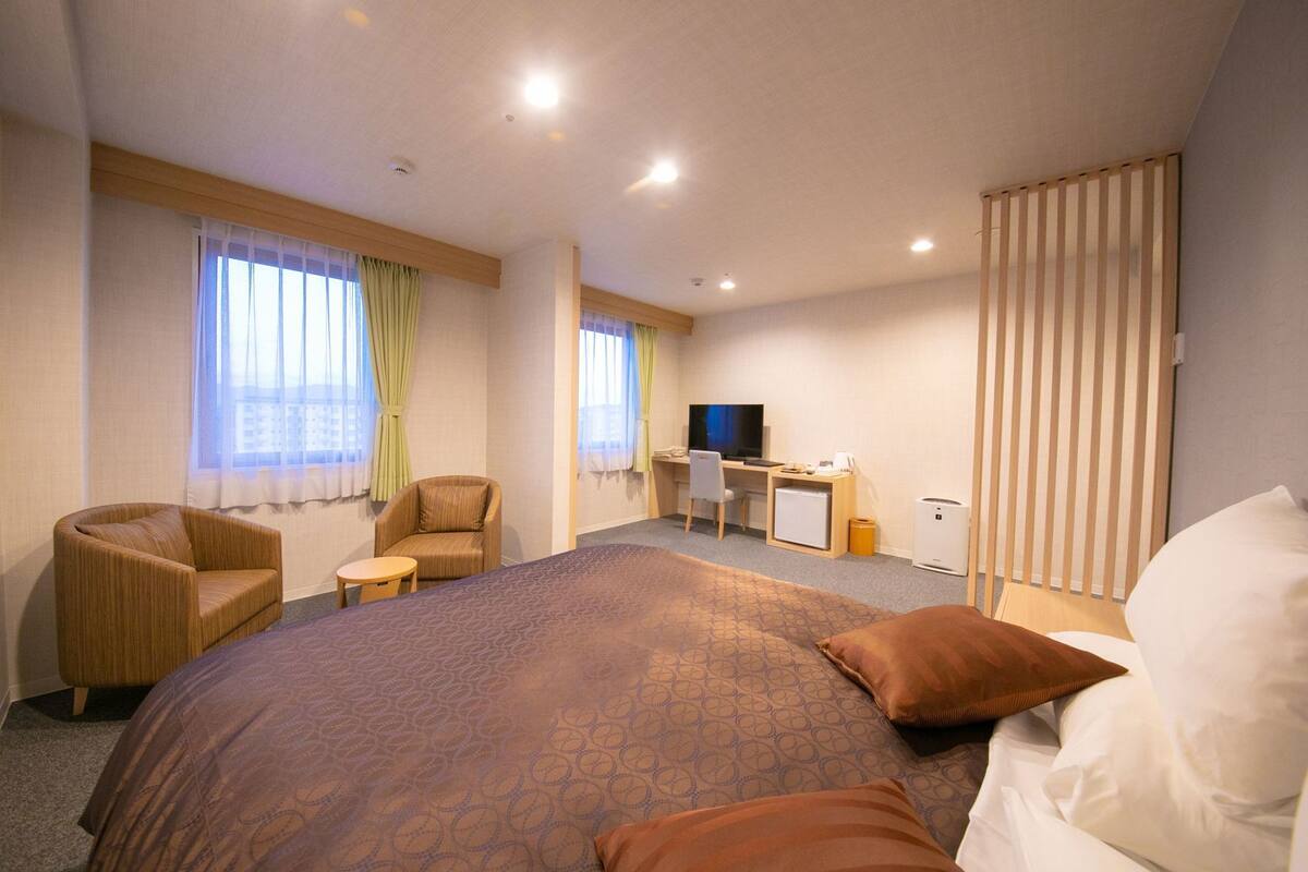A hotel room with a large bed, a desk with a computer, a chair, and a television.