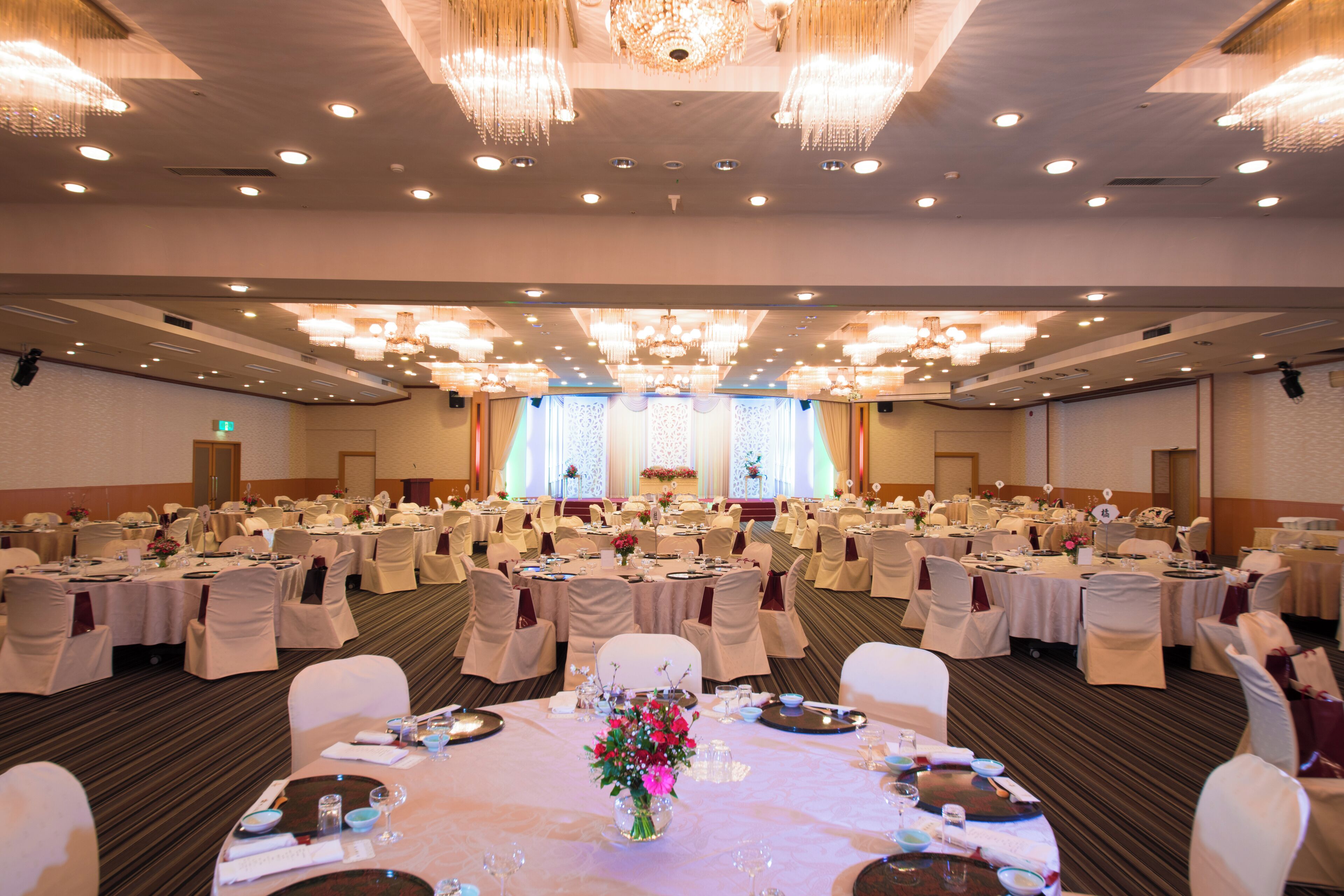 Uma sala de banquetes com mesas redondas, toalhas brancas e cadeiras.