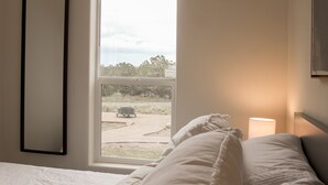 A bedroom with a bed, a bedside lamp, a window with a view of a garden and a vehicle outside. - NEW!  THE RETREAT Ranch House - Only 20 minutes from the Grand Canyon (Williams)