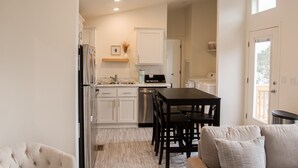 A modern kitchen with white cabinetry, a dining area with a black table and chairs, and a cozy seating area with a tufted sofa. - NEW!  THE RETREAT Ranch House - Only 20 minutes from the Grand Canyon (Williams)