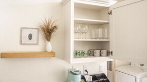 A laundry area with a white washing machine, a drying rack, and a shelf with glassware and a vase of dried plants. - NEW!  THE RETREAT Ranch House - Only 20 minutes from the Grand Canyon (Williams)