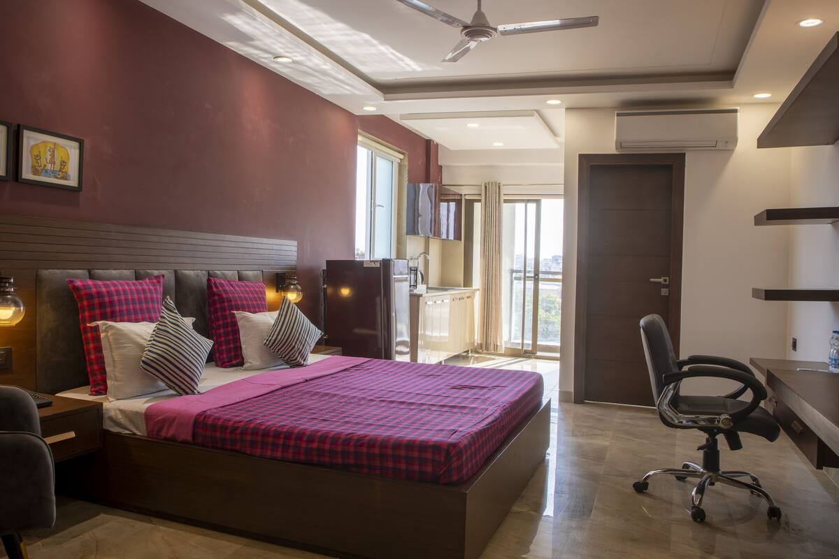 A modern bedroom with a bed, a desk, a chair, a ceiling fan, and a window.
