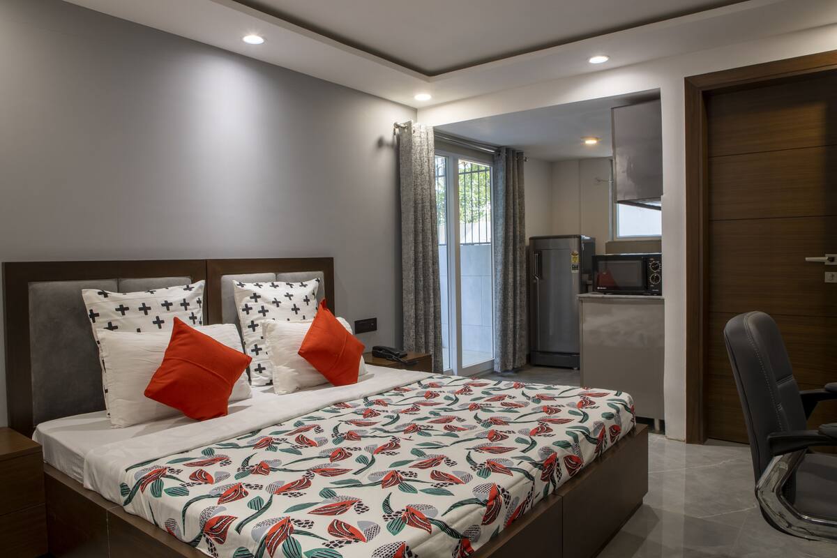 A modern bedroom with a large bed, a desk, and a kitchenette.