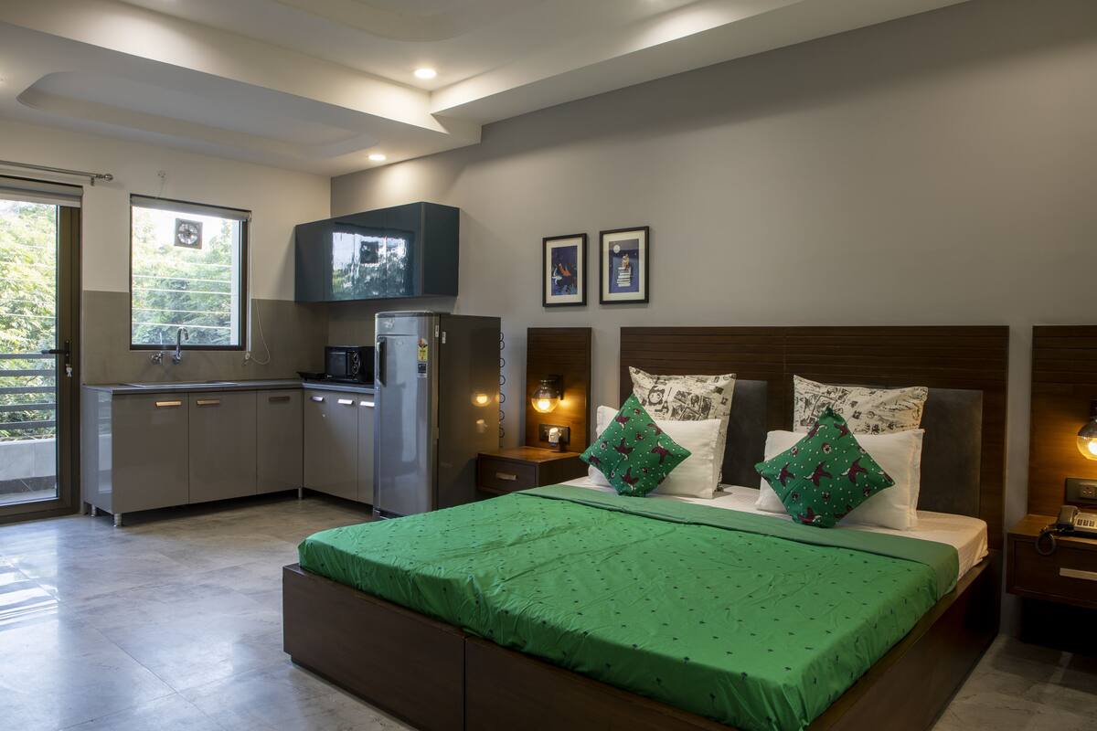 A bedroom with a bed, nightstands, a TV, and a kitchenette.