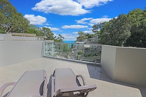 Enjoy the ocean view from this outdoor space with lounge chairs and a glass balustrade.