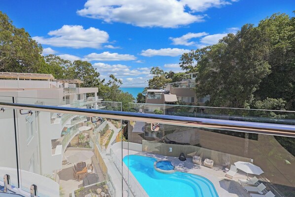 Enjoy a serene view of the pool and ocean from the spacious balcony with a glass railing.