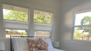 A bedroom with a bed, two bedside tables, a window, and a view of greenery outside.