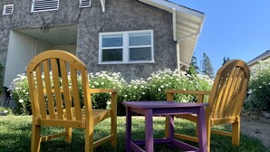 A house with a grey exterior, a window, and two wooden chairs with a small table in front.