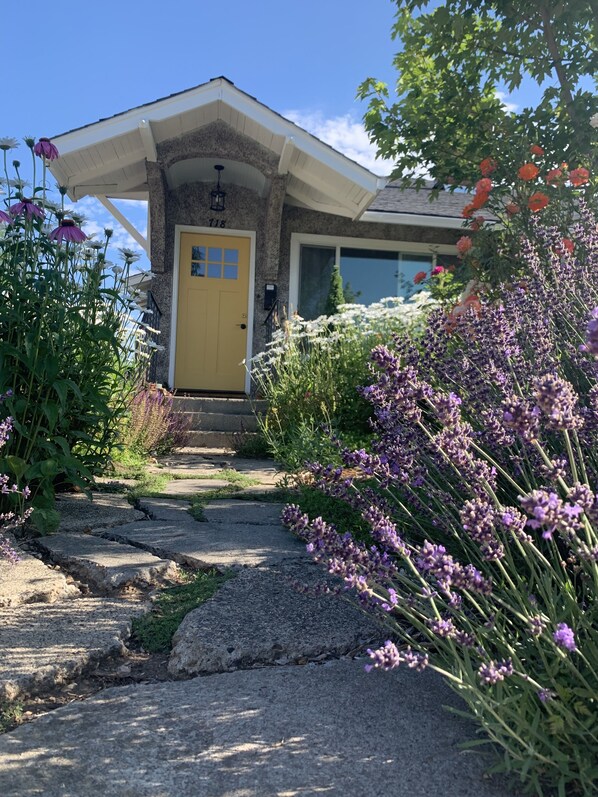 A house with a yellow door, a stone facade, and a garden with various flowers.