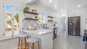 A modern kitchen with white cabinetry, a large island with stools, a stainless steel refrigerator, and patterned backsplash tiles.