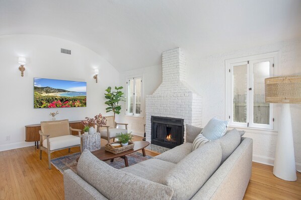 A living room with a white brick fireplace, a large painting, and a sofa. - Belmont Shore Bungalow (Long Beach)