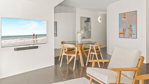 A modern living room with a flat-screen TV, wooden chairs, a glass table, and artwork on the walls. - Penthouse 20 - The Cove (Noosa)